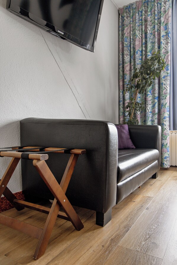 Una sala de estar moderna con un sofá de cuero, una mesa de centro de madera, un televisor de pantalla plana montado en la pared y una planta en maceta.