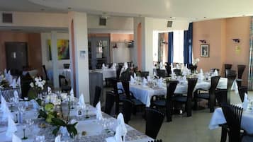Een restaurant met meerdere eettafels gedekt voor gasten, met witte tafellinnen en zwarte stoelen.