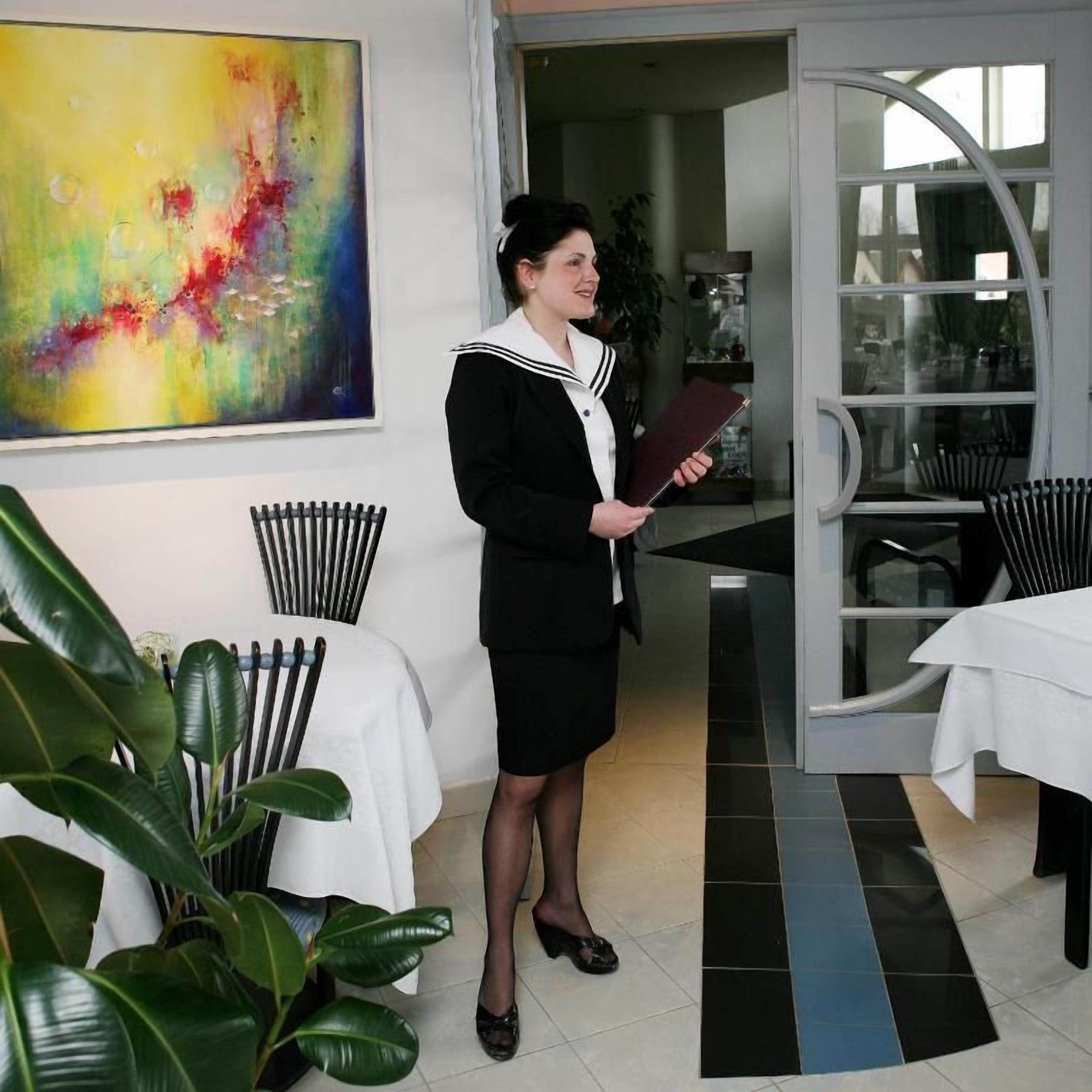 Una persona de pie en una habitación con una mesa blanca, sillas y un cuadro abstracto grande en la pared.