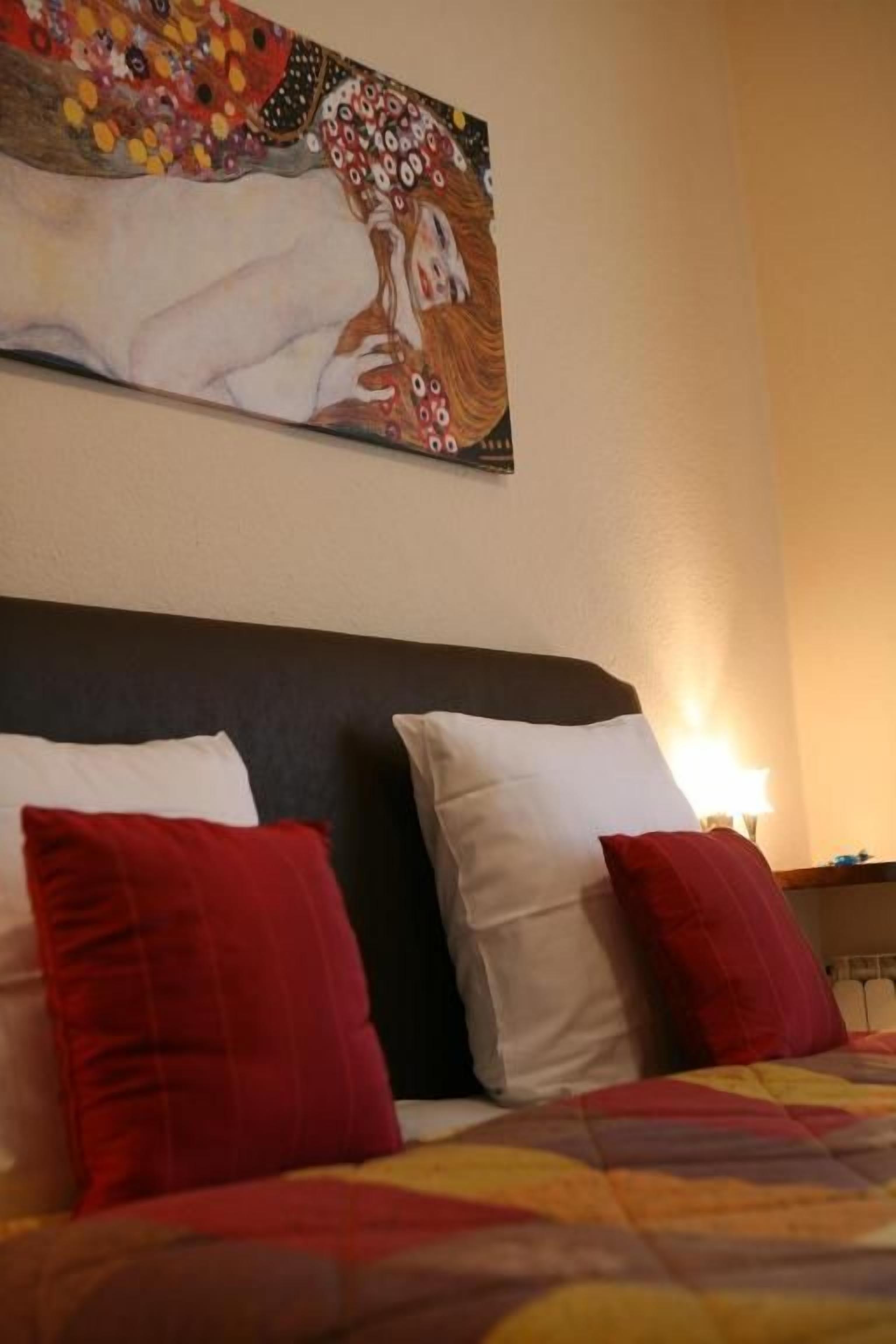 Un lit avec des oreillers rouges et blancs, une couvre-lit à motifs et un tableau au-dessus de la tête de lit.