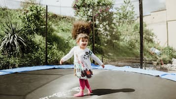 Een kind springt op een trampoline, omringd door groen.
