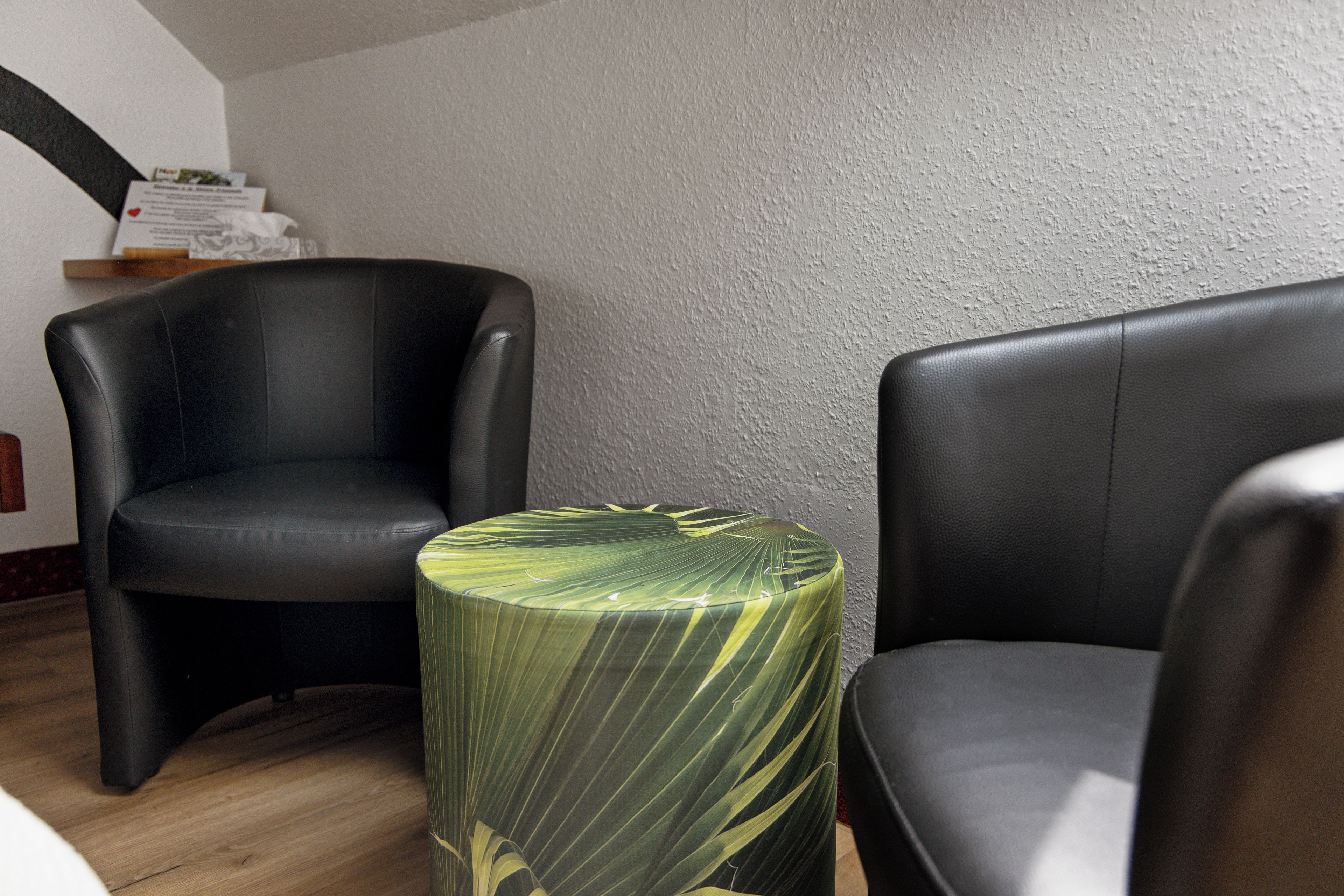 A room with two black leather chairs, a round table with a green leaf pattern, and a textured wall.