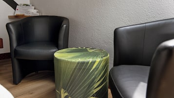 A room with two black leather chairs, a round table with a green leaf pattern, and a textured wall.