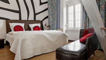 Un dormitorio con cama, un banco, una ventana y un papel tapiz estampado.
