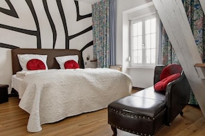 Un dormitorio con cama, un banco, una ventana y un papel tapiz estampado.