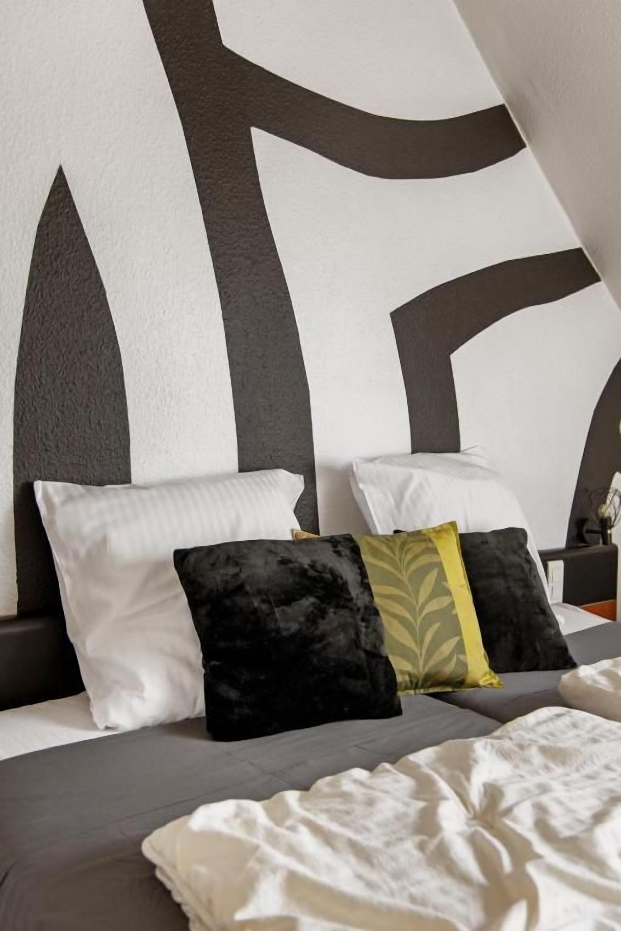 Un lit avec une tête de lit blanche et grise, plusieurs oreillers et une couverture blanche.