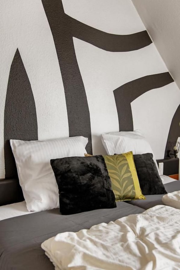 A bed with a white and gray headboard, multiple pillows, and a white blanket. - Maison Ernenwein (Obermodern-Zutzendorf)