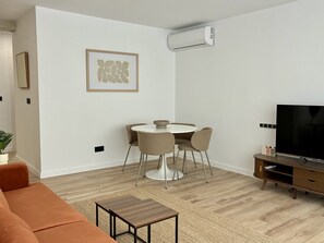 A modern living room with a sofa, a dining table with chairs, a TV, and a wall-mounted air conditioner. - Modern apartment with a terrace in Malvarrosa, Valencia Beach (València)