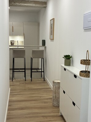 A modern kitchen with white cabinets, two bar stools, a small plant, and a trash bin. - Modern apartment with a terrace in Malvarrosa, Valencia Beach (València)
