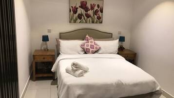 A hotel room with a bed, two bedside tables, a headboard, a wall-mounted painting, and a folded towel on the bed.