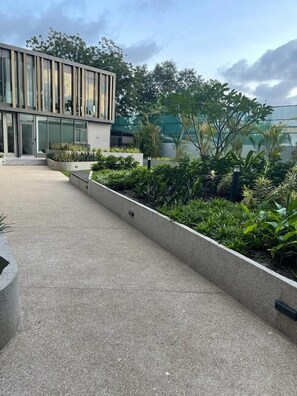Um edifício moderno com telhado plano, grandes janelas e área ajardinada com diversas plantas.