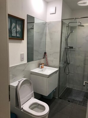 A bathroom with a toilet, sink, mirror, and shower. - The Lennox Apartments-Airport (Accra)