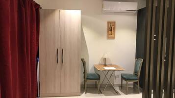 A room with a wooden wardrobe, a table with two chairs, and an air conditioning unit on the wall.