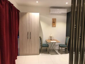 A room with a wooden wardrobe, a table with two chairs, and an air conditioning unit on the wall. - The Lennox Apartments-Airport (Accra)