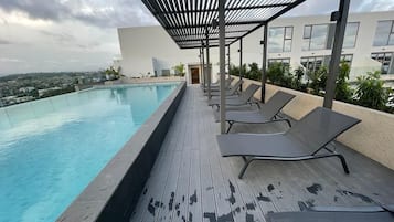 A rooftop pool with lounge chairs, a pergola, and a city view.