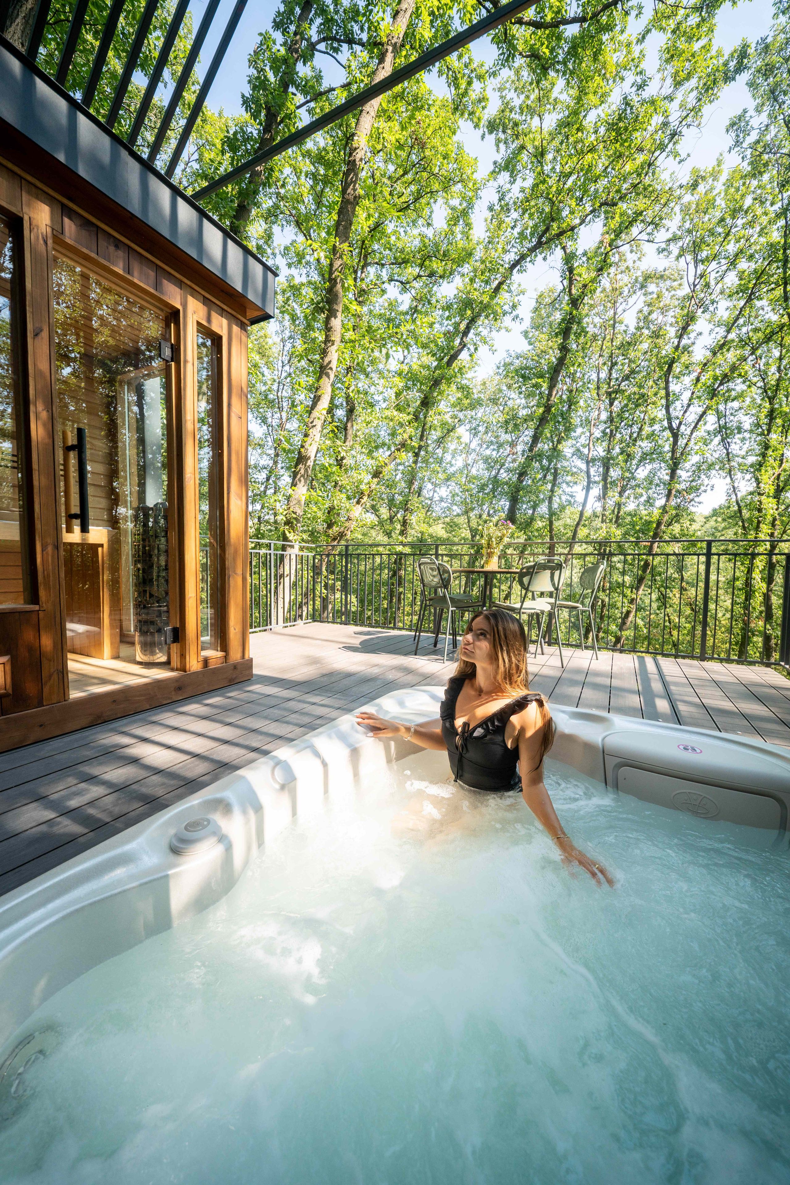 Iemand ontspant in een jacuzzi met een houten terras en glazen deuren die naar een kamer leiden.