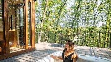Iemand ontspant in een jacuzzi met een houten terras en glazen deuren die naar een kamer leiden.