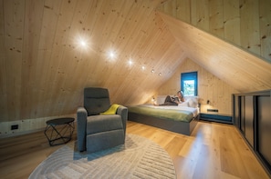 A cozy attic bedroom with a sloped ceiling, a single bed, a reading chair, and a small table.