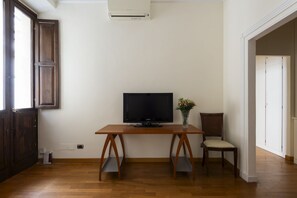 A room with a wooden desk, a television, a chair, and a vase with flowers. - Porta Pia Enchanting Apartment (Roma)