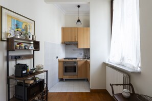A compact kitchen with wooden cabinets, a built-in oven, and a window with sheer curtains. - Porta Pia Enchanting Apartment (Roma)