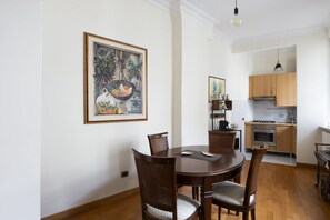 A dining area with a round table and chairs, a kitchen in the background, and a framed artwork on the wall. - Porta Pia Enchanting Apartment (Roma)