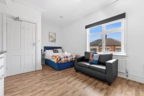A bedroom with a bed, a sofa, a window, and a door. - Beautiful studio near Leeds City Centre - Room 6 (Leeds)
