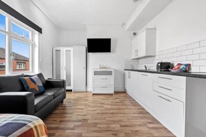 A modern kitchen with white cabinetry, a black countertop, and a television mounted above the sink. - Beautiful studio near Leeds City Centre - Room 6 (Leeds)