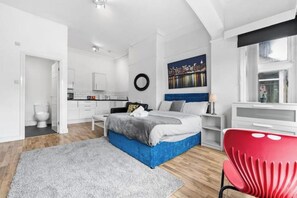 Ein modernes Schlafzimmer mit einem Bett, einem roten Sessel, einem Stadtbildgemälde und Blick auf die Stadt durch ein Fenster.