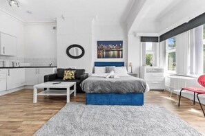 Ein modernes Schlafzimmer mit einem Bett, einem Sofa, einem Couchtisch und Blick auf die Stadt durch große Fenster.