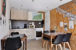 Cocina compacta con armarios de madera, microondas, cafetera y comedor con mesa y sillas.