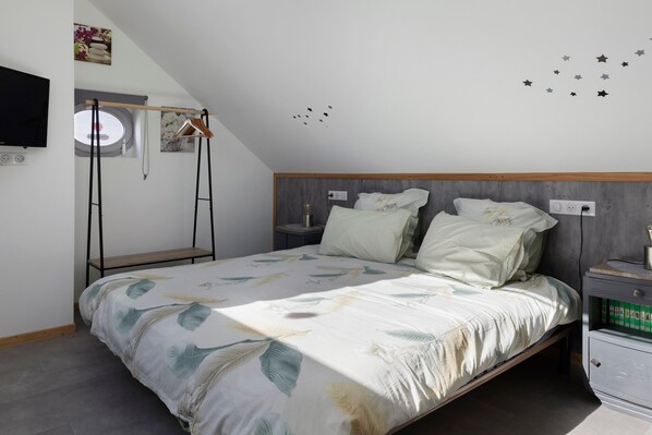 Un dormitorio con cama, mesita de noche, cómoda, ventana, televisor instalado en la pared y ventilador de techo.