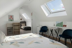 Un dormitorio con cama, escritorio, dos sillas, estantería y tragaluz.