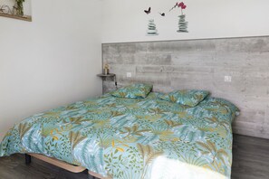 A bedroom with a bed, a nightstand, a wall-mounted shelf, and a decorative wall art piece. - Cottage 'L'ancienne Forge' with Private Terrace, Private Garden and Wi-Fi (Louvetot)