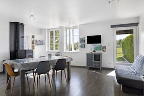 A modern kitchen with a dining area, a flat-screen TV, and a view of the outdoors. - Cottage 'L'ancienne Forge' with Private Terrace, Private Garden and Wi-Fi (Louvetot)
