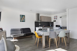 A modern kitchen with a dining table, chairs, and a sofa. - Cottage 'L'ancienne Forge' with Private Terrace, Private Garden and Wi-Fi (Louvetot)