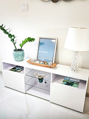 Ein weißes Konsolentische mit einem gerahmten Bild, einer Topfpflanze, Dekorationsgegenständen und einer Lampe.