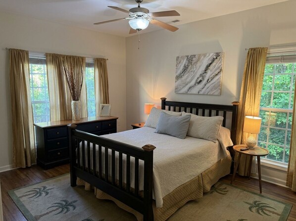 A bedroom with a bed, nightstands, a ceiling fan, a window with curtains, and a wall-mounted artwork.