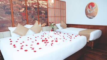 A hotel room with a bed adorned with red rose petals, a traditional Asian-style wall painting, and a round painting of cranes.