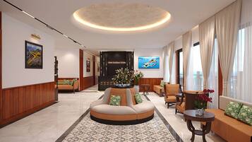 A hotel lobby with a round seating area, a reception desk, and a large TV screen.