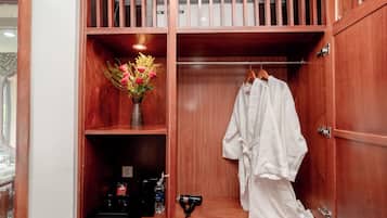 A wooden wardrobe with a hanging robe and a vase of flowers on the top shelf.