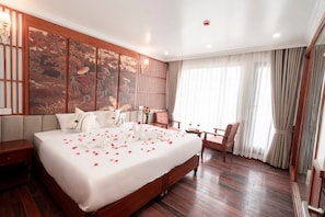 A hotel room with a large bed, wooden flooring, a decorative wall, and a view of the outdoors. - Daiichi Luxury Cruise (Hai Phong)