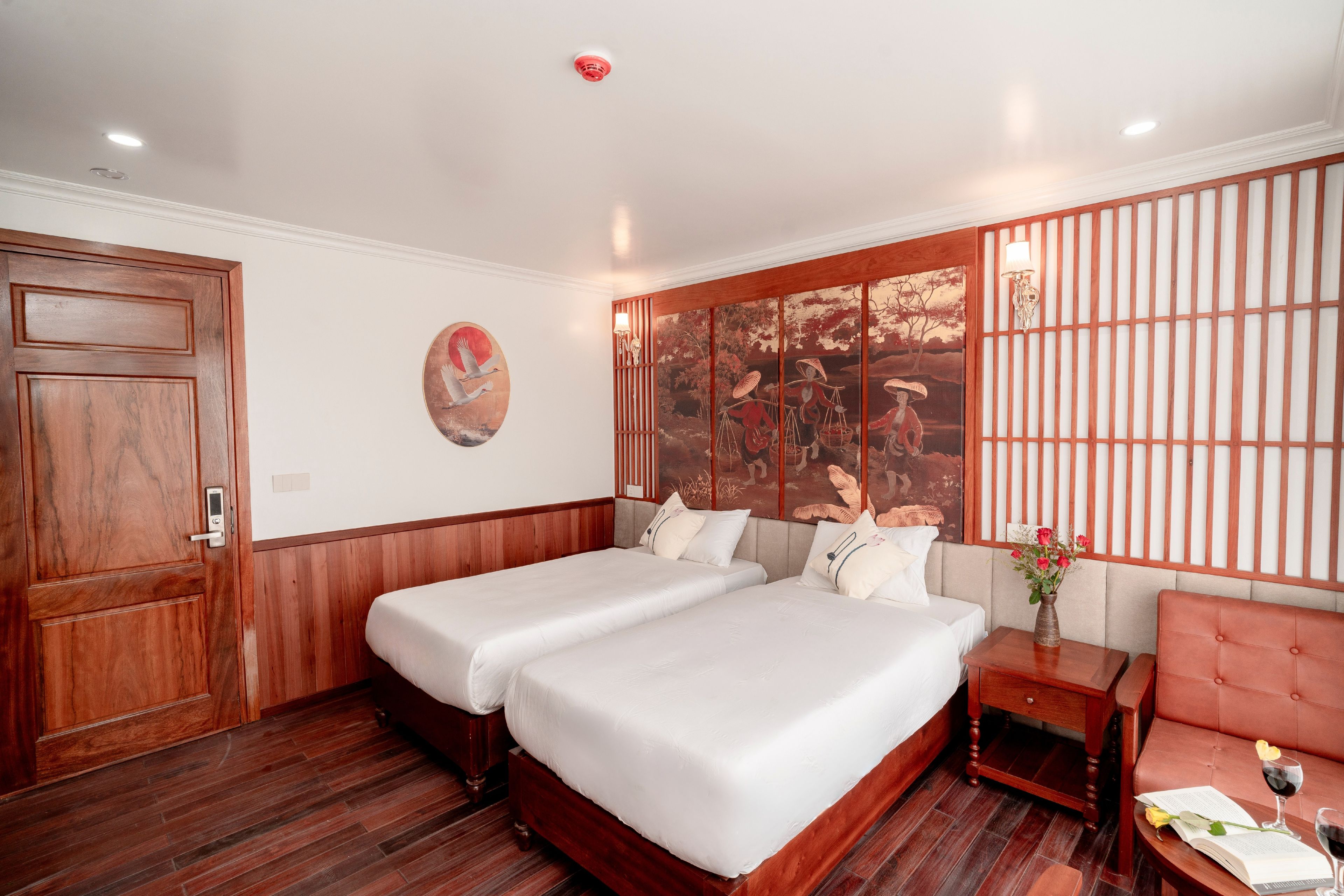 A hotel room with two beds, a wooden door, a wall-mounted artwork, and a traditional-style partition.