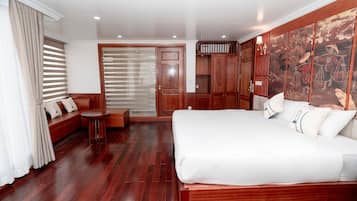 Una camera d'albergo con un letto grande, un'area salotto con un tavolo e una porta scorrevole che dà su un balcone.