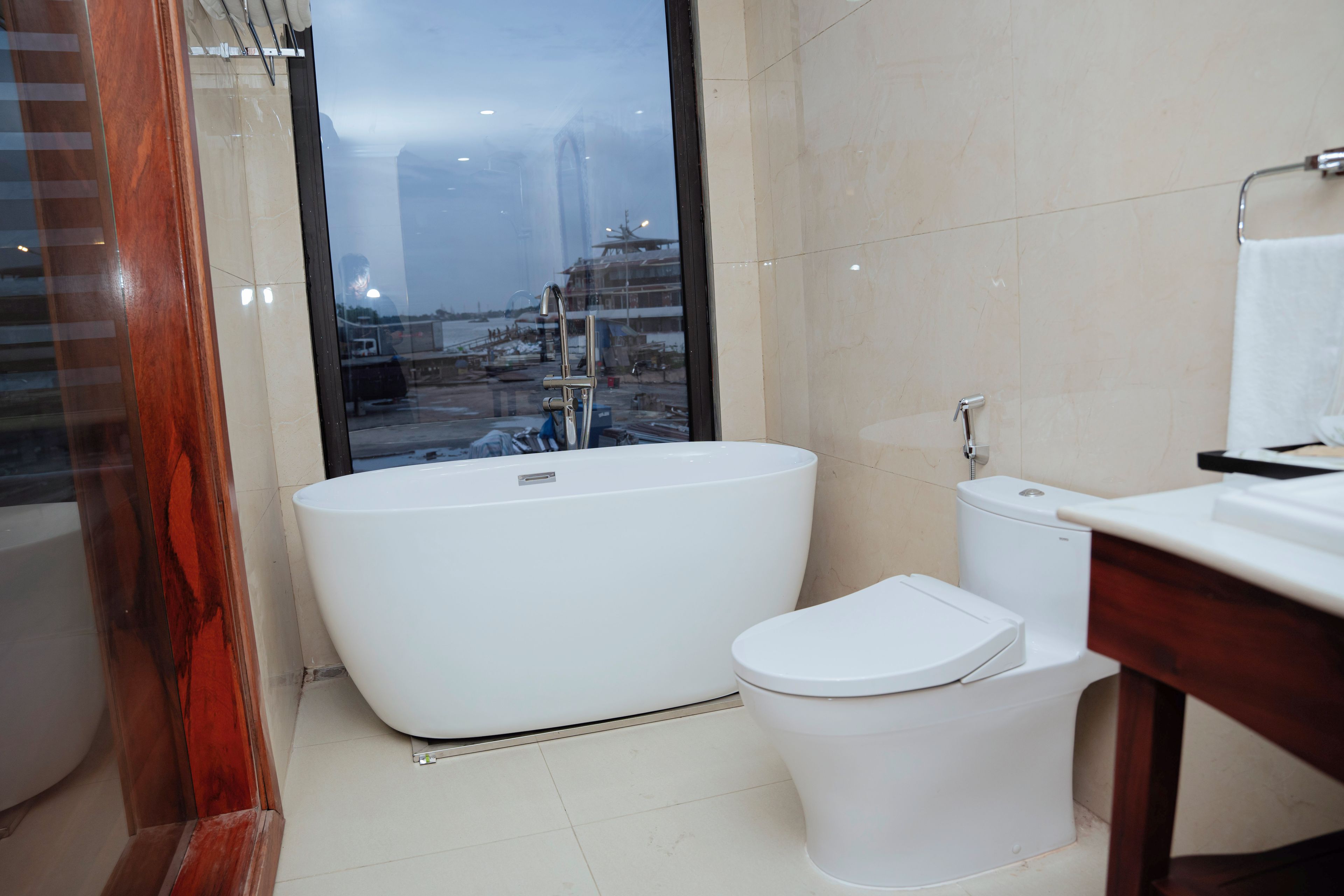 Une salle de bain moderne avec une baignoire sur pieds, des toilettes et une grande fenêtre donnant sur un paysage urbain.
