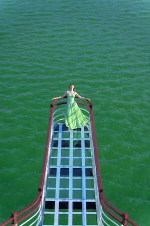 A person in a green dress standing on a bridge with a railing, overlooking a body of water. - Daiichi Luxury Cruise (Hai Phong)