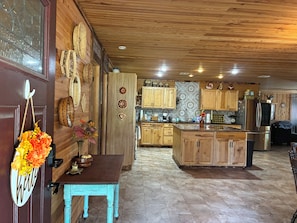 A spacious kitchen with wooden cabinets, a central island, and a rustic ceiling. - The Killabrew Cabin Hot Tub & Country Escape (Hulbert)