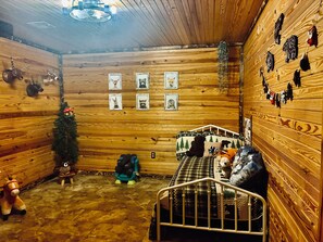 A cozy room with wooden walls, a bed with a metal frame, a small table, and various wall decorations including framed pictures and stuffed animals.