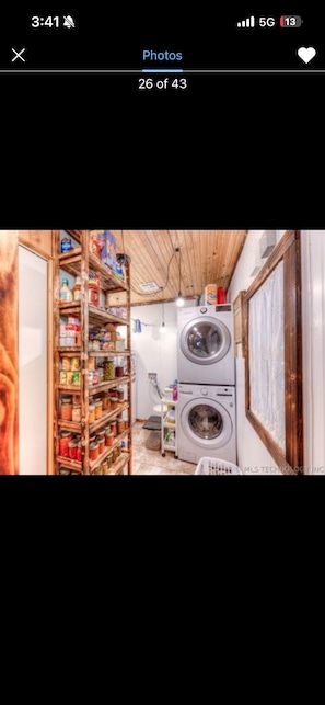 A laundry area with stacked washing machines and a wooden shelf filled with various items. - The Killabrew Cabin Hot Tub & Country Escape (Hulbert)