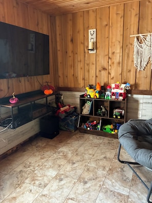 A room with a television mounted on the wall, a wooden floor, and shelves with various toys and decorations. - The Killabrew Cabin Hot Tub & Country Escape (Hulbert)