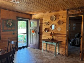 A wooden interior with a door, a table with a vase, and a chair.